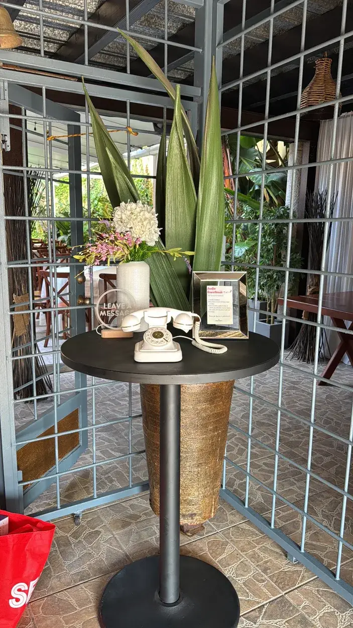 Teléfono retro blanco de Audio Guest Book sobre una mesa, con flores y plantas alrededor